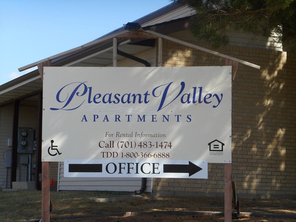 A sign for Pleasant Valley Apartments with a handicap symbol and an arrow pointing to the office.