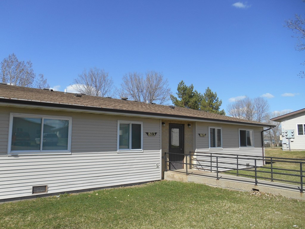 A house with a brown roof and a grey siding with a black door and a small porch.