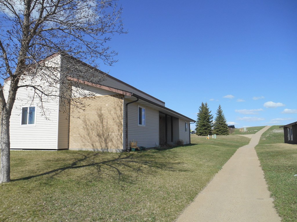 A building with a white and beige exterior is surrounded by a grassy area and a clear blue sky.