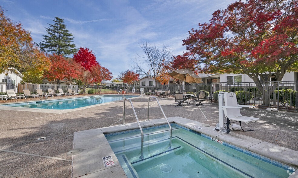a pool with a hot tub and chairs in a yard with trees