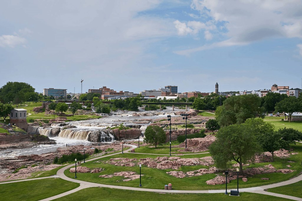 A waterfall in a park with a city in the background.
