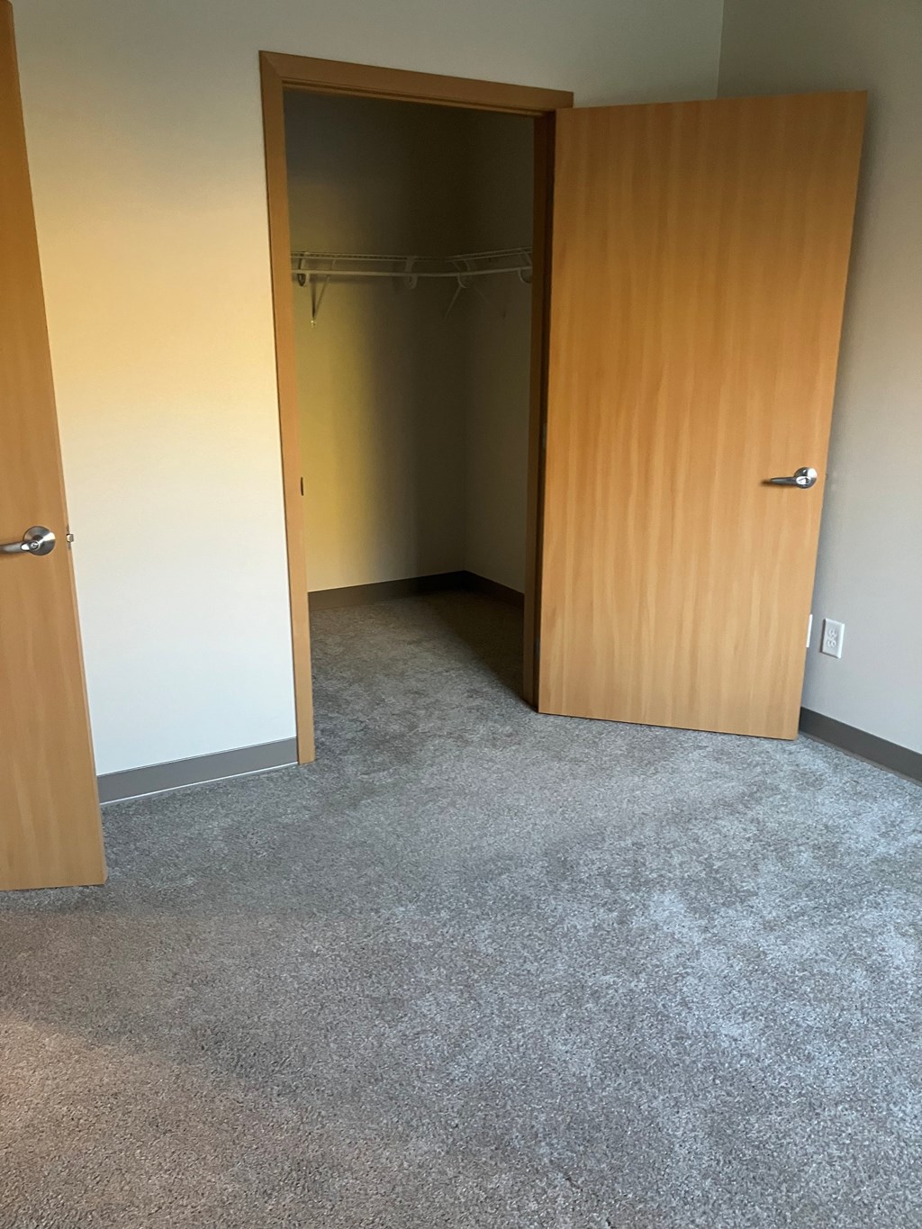 A room with a wooden door and a grey carpet.