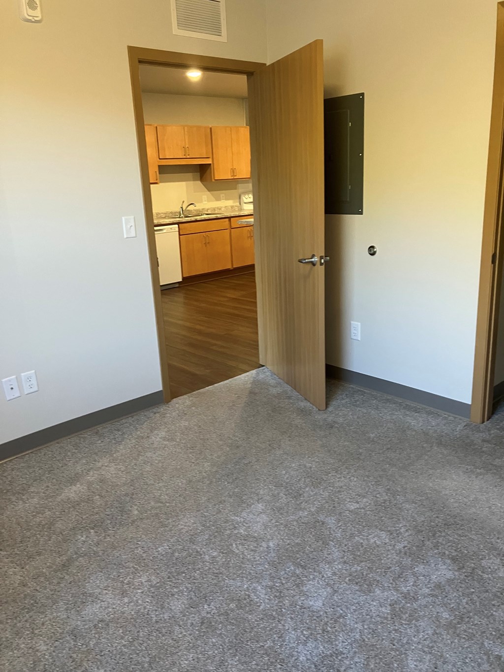A room with a carpeted floor and a doorway leading to a kitchen.