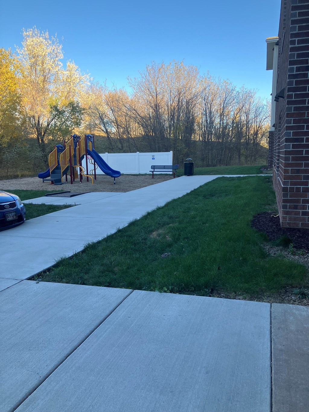 A playground with a yellow slide and a blue car parked in the driveway.