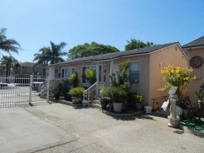 a small building with a white gate and plants in front of it