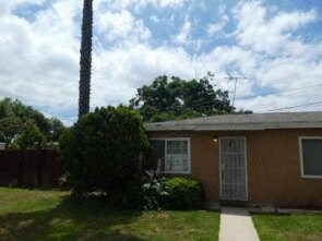 a small brown house with a sidewalk and a palm tree