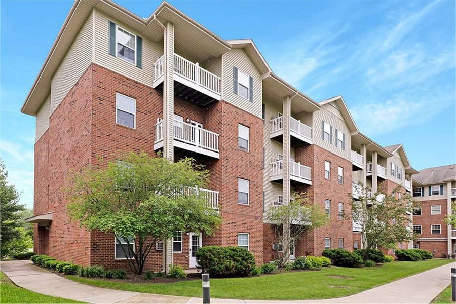 A red brick apartment building with balconies and trees in front.