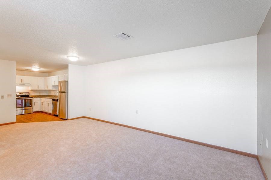 A large empty room with a kitchen visible in the background.