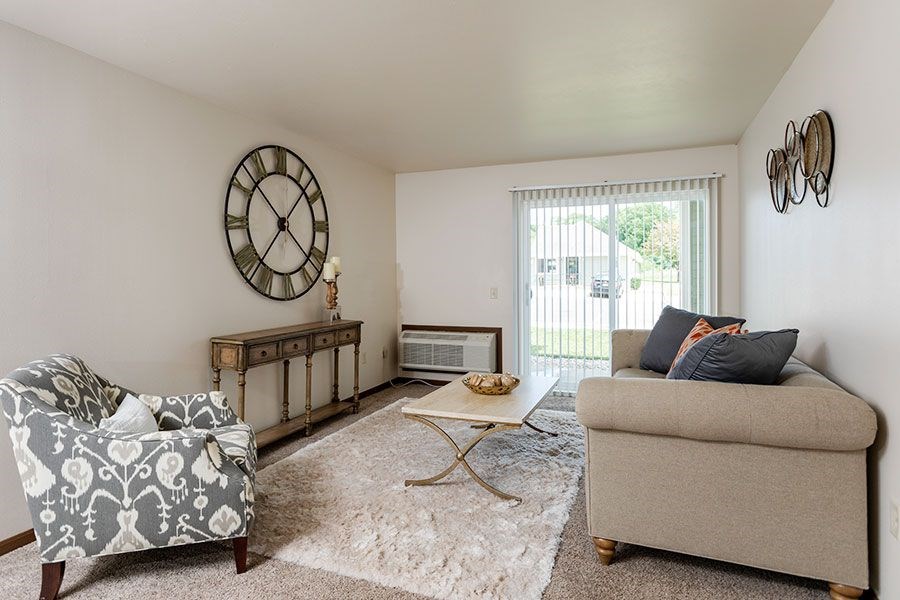 A living room with a grey sofa, a chair, a coffee table, and a clock on the wall.