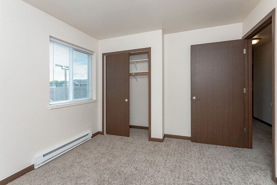 A room with a carpeted floor, two doors, and a window with blinds.