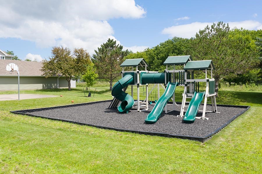 A playground with a green slide and a grey mat.