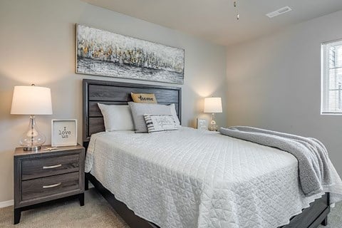 A bedroom with a large bed, a nightstand with a lamp, and a framed picture on the wall.