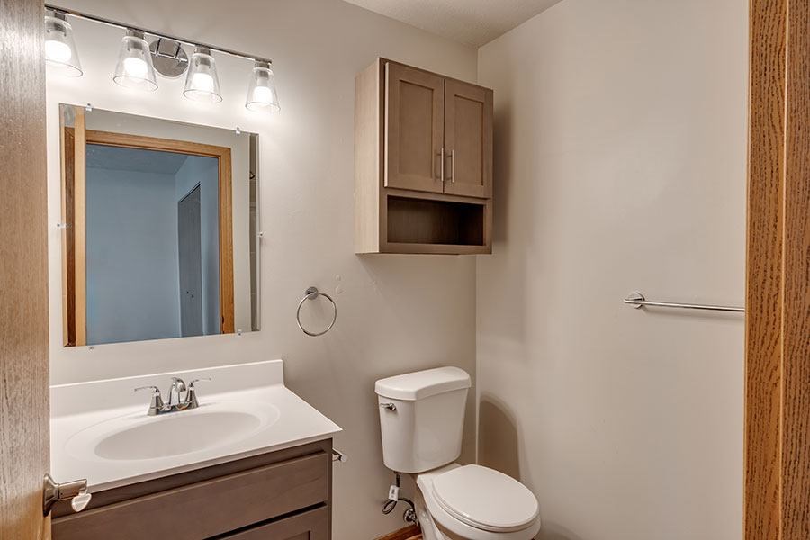 A bathroom with a toilet, sink, mirror, and lighting fixture.