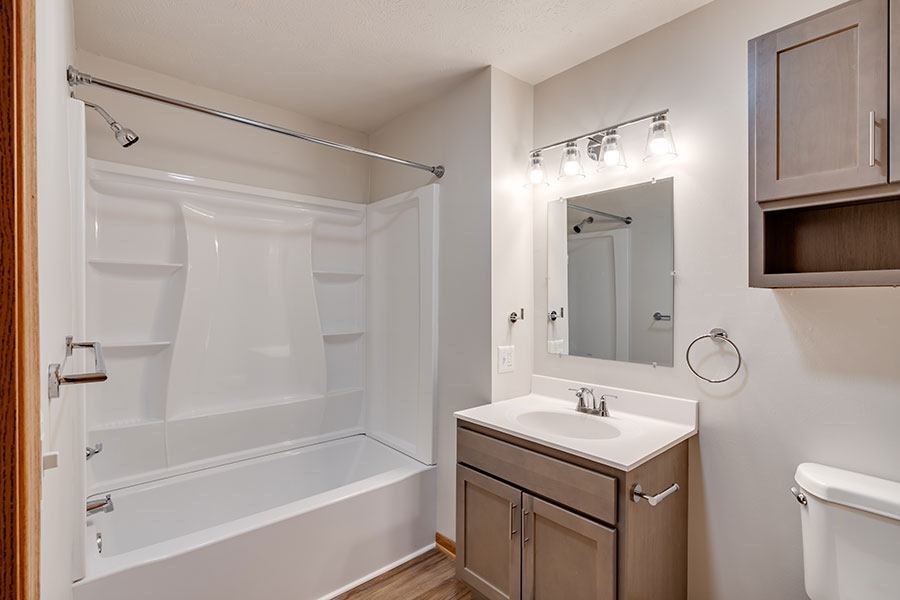 A white bathroom with a walk-in shower, sink, and mirror.