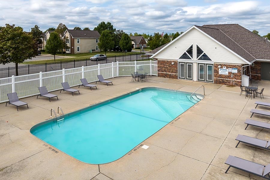 A large outdoor swimming pool surrounded by a white fence and lounge chairs.