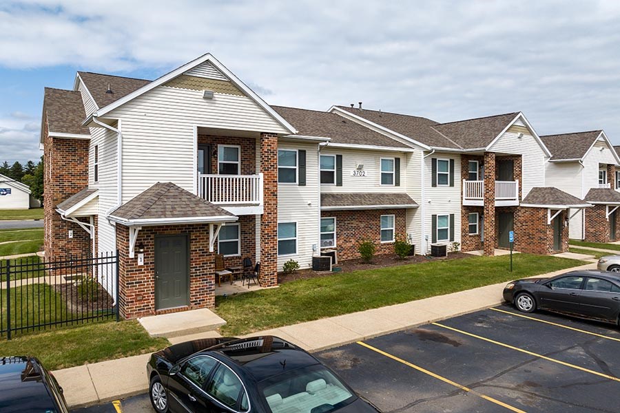 A black car is parked in a parking lot in front of a brick building.