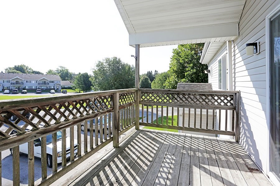 A wooden deck with a railing and a white house in the background.