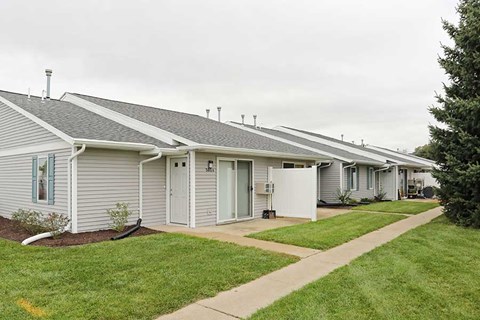 a row of white houses with a sidewalk and grass