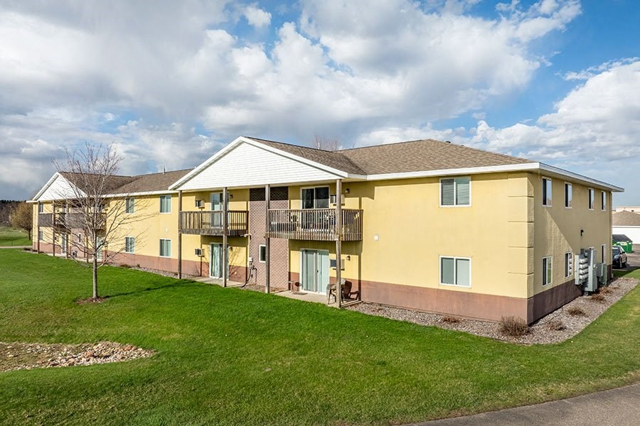 a yellow apartment building with a green yard and a cloudy sky