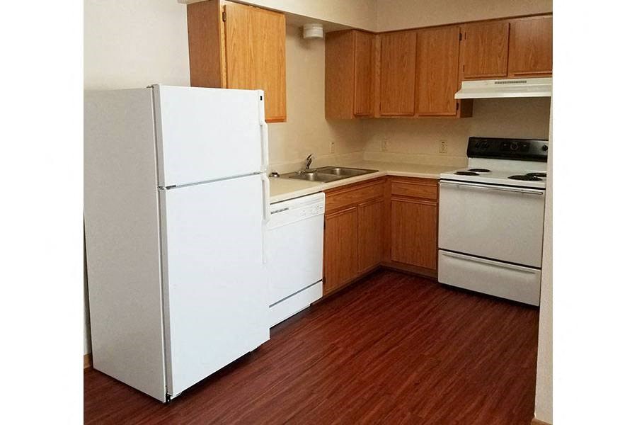 A white refrigerator stands in a kitchen with wooden cabinets and a white stove.
