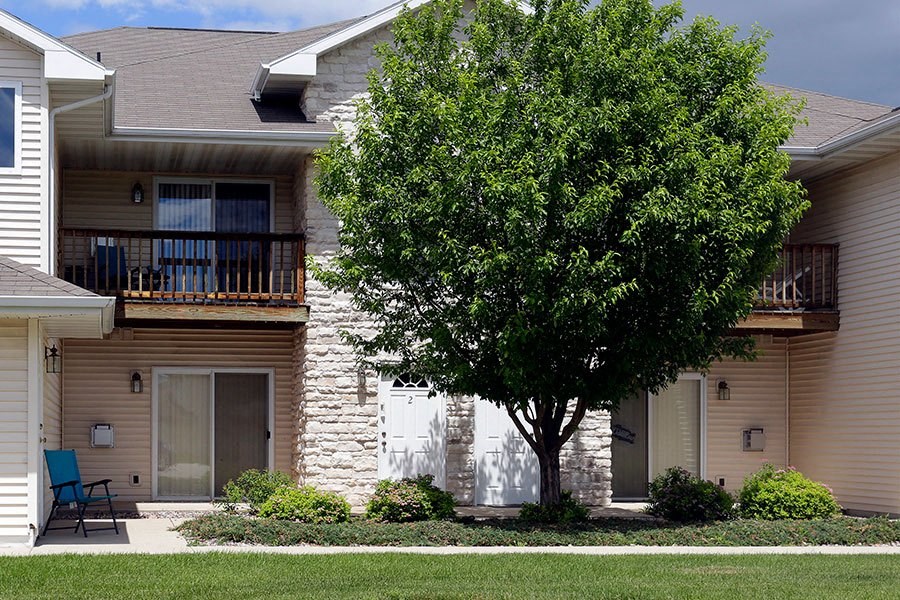 A tree in front of a tan building with a white fence.