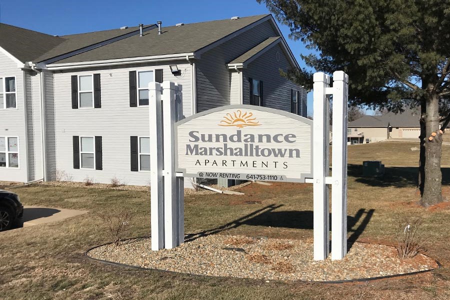 A sign for Sundance Marshaltown Apartments stands in front of a building.