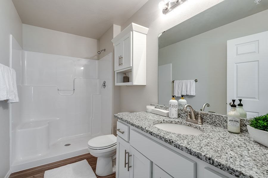 A white bathroom with a marble counter top and a white toilet.