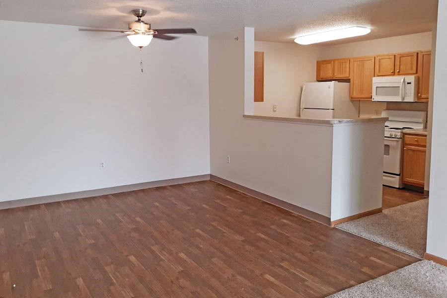 an empty living room with a kitchen and a ceiling fan