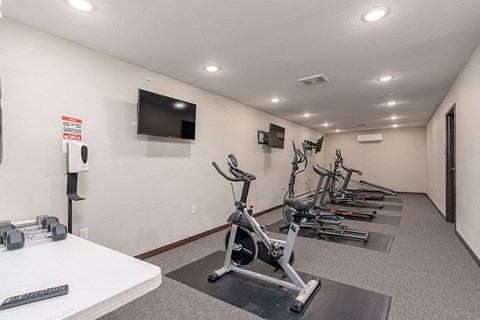 A gym room with a row of stationary bikes and a TV mounted on the wall.