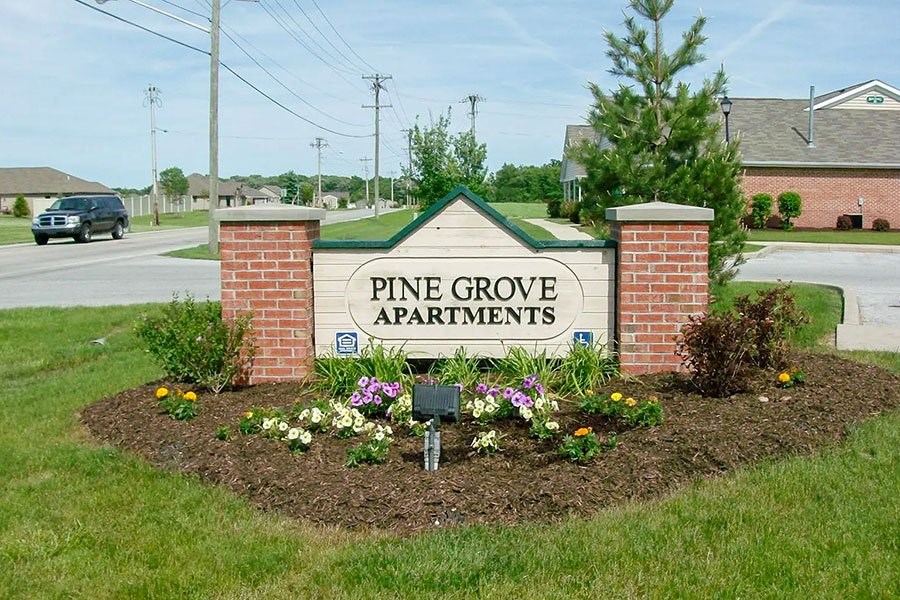 A sign for Pine Grove Apartments is surrounded by flowers.