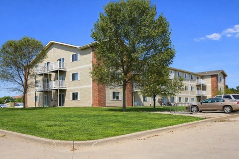 Apartment building with a tree in front and a car parked in the driveway.