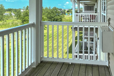 A white deck with a view of a green lawn and trees.