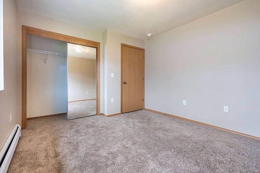 A room with a carpeted floor, a mirror, and a door.