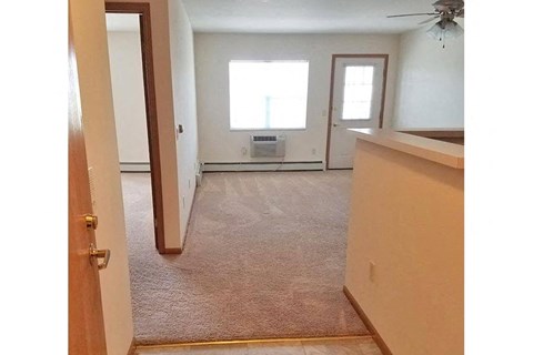 an empty living room with a kitchen and a window