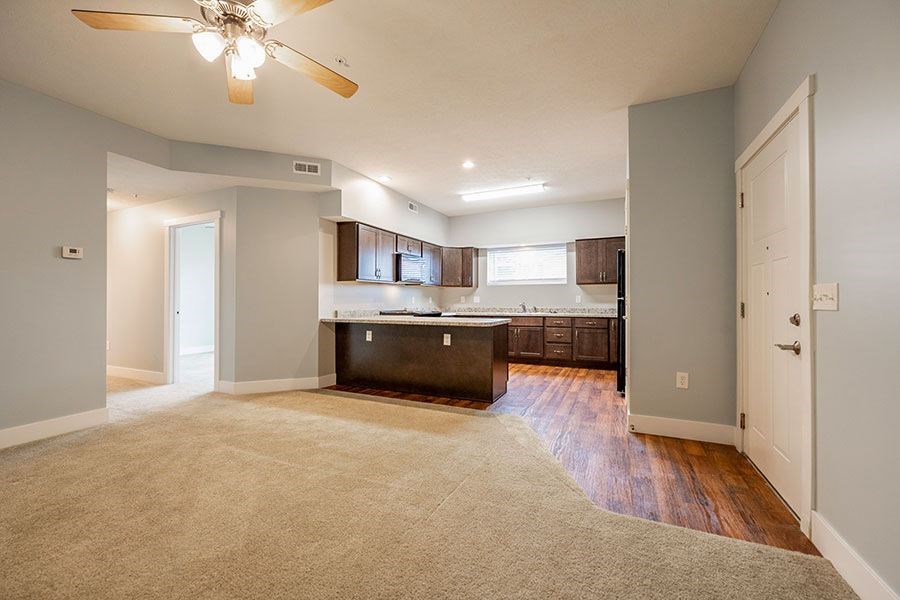 A spacious living room with a kitchen area in the background.