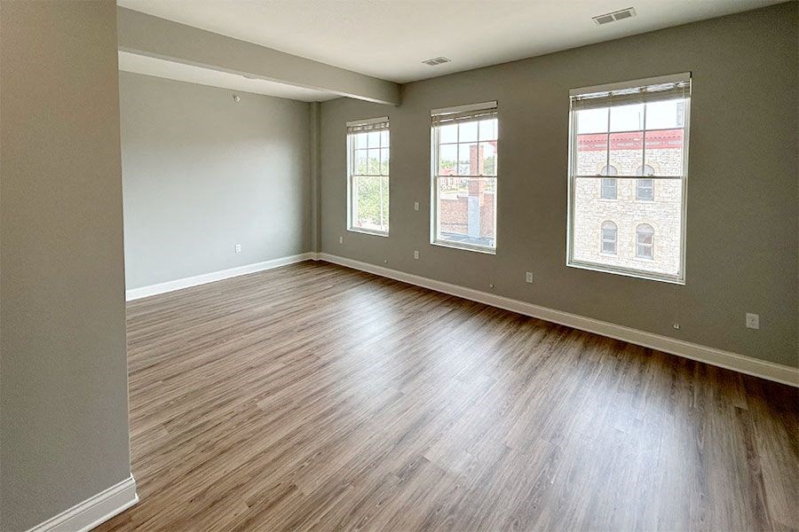 an empty living room with wood flooring and three windows