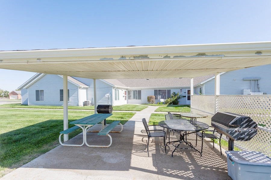 a patio with a picnic table and chairs and a grill