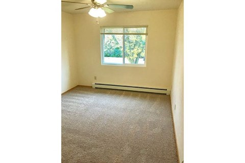 an empty bedroom with a window and a ceiling fan