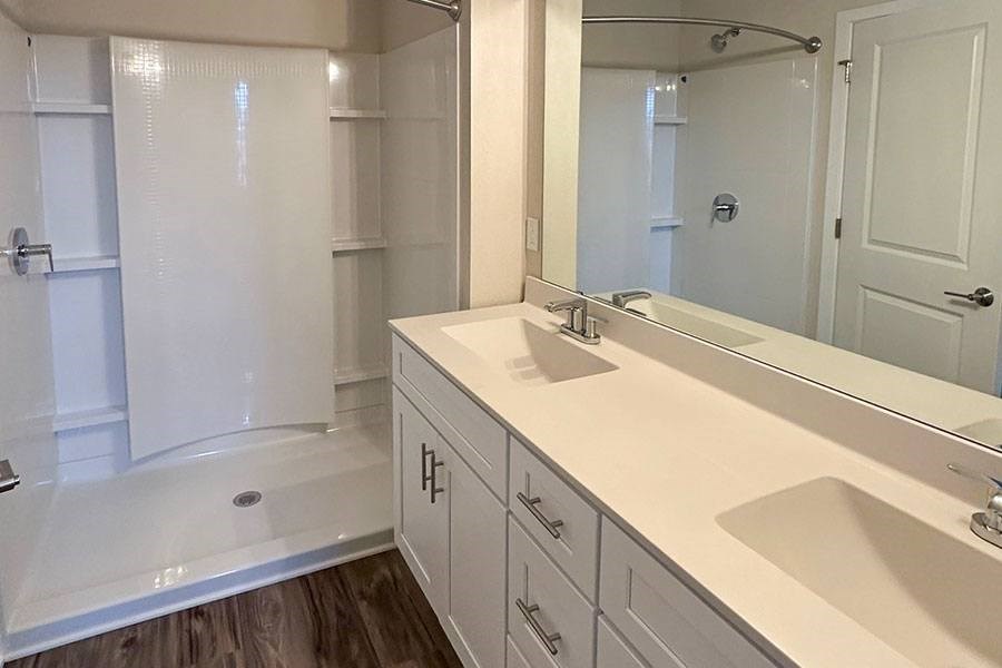 A white bathroom with a sink, mirror, and shower.