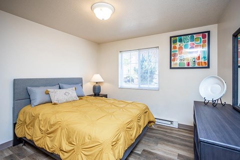 A bedroom with a yellow bedspread and a painting on the wall.
