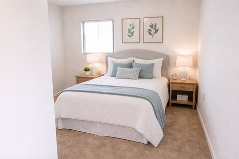 A bedroom with a bed, two lamps, and two framed leaves on the wall.
