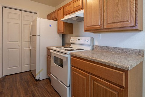 A kitchen with a white fridge, white stove, and wooden cabinets.