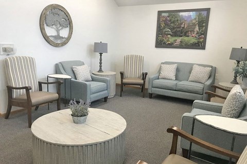 A living room with a grey couch, a white table, and a painting on the wall.