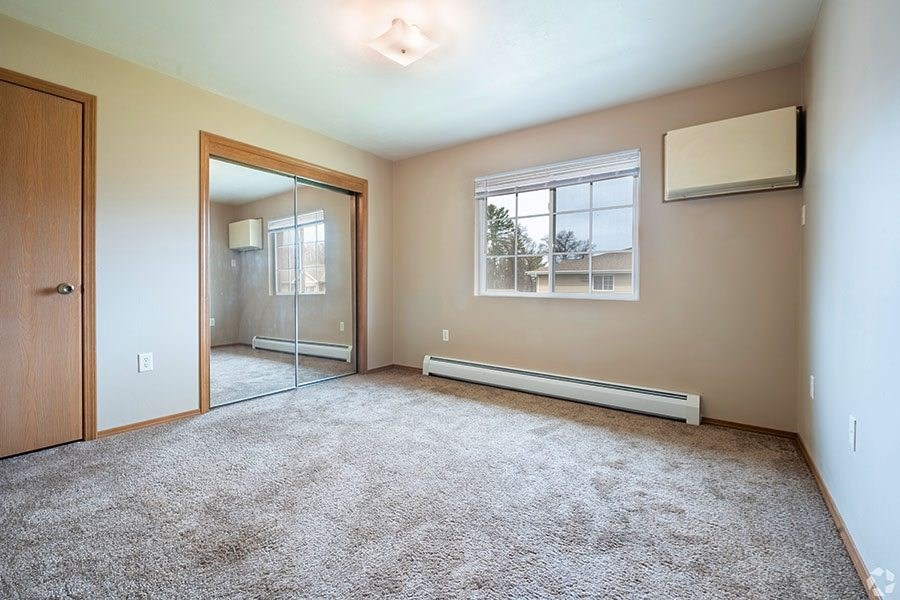 A room with a carpeted floor, a window, and a door.
