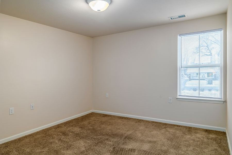 A room with a carpeted floor and a window with blinds.