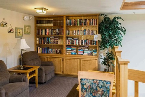 A living room with a bookshelf, a chair, a table, and a lamp.