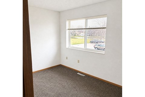 A room with a window showing a view of a parking lot and trees.