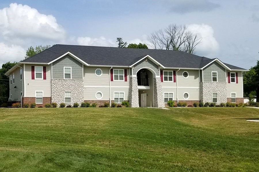 A house with a grey and red facade stands in a grassy field.