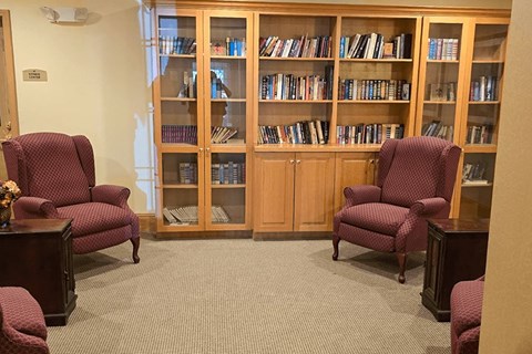 A room with a bookcase and two chairs.