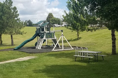 A playground with a green slide and picnic tables.